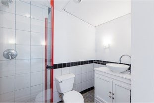 full bath with tile walls, a shower stall, toilet, and vanity