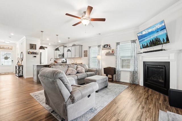 living room featuring crown molding, a glass covered fireplace, plenty of natural light, recessed lighting, and a ceiling fan