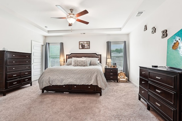 bedroom with visible vents, a ceiling fan, a tray ceiling, and light carpet