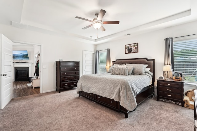 carpeted bedroom with ceiling fan, visible vents, a glass covered fireplace, and a raised ceiling