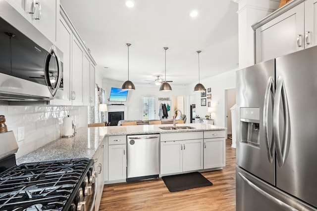 kitchen featuring ceiling fan, a sink, a fireplace, stainless steel appliances, and a peninsula