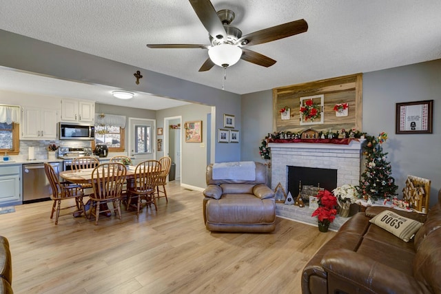 living room with ceiling fan, a fireplace, a textured ceiling, and light hardwood / wood-style flooring