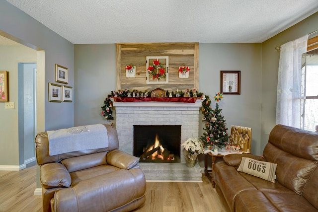 living room with a textured ceiling, light wood-type flooring, a brick fireplace, and plenty of natural light