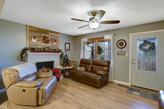 living room featuring a textured ceiling, light hardwood / wood-style floors, a brick fireplace, and ceiling fan