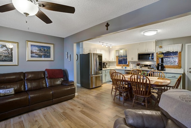 dining area with rail lighting, ceiling fan, light wood-type flooring, and a textured ceiling