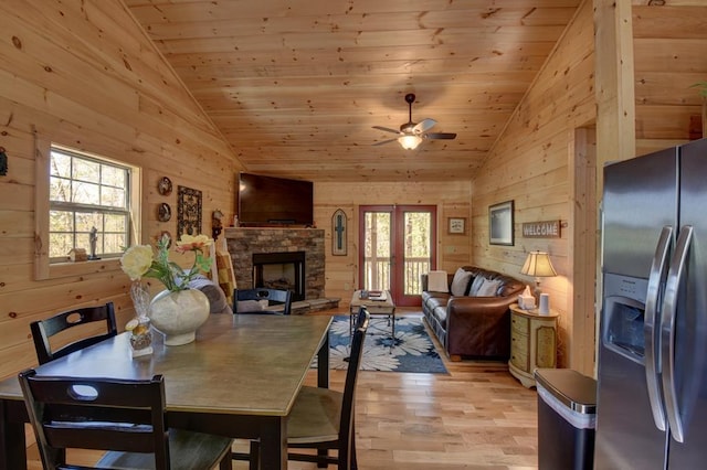 dining space featuring vaulted ceiling, wooden walls, light hardwood / wood-style flooring, wooden ceiling, and a stone fireplace