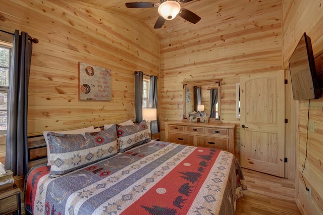 bedroom with wooden walls, light hardwood / wood-style floors, ceiling fan, and lofted ceiling