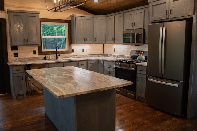 kitchen with sink, stainless steel appliances, dark hardwood / wood-style floors, light stone countertops, and a kitchen island