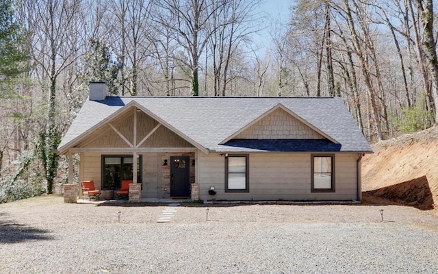 view of front facade with covered porch, a shingled roof, and a chimney