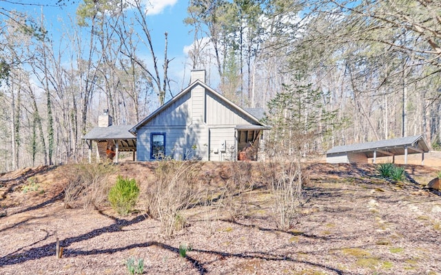 rear view of house featuring a wooded view, a chimney, and board and batten siding