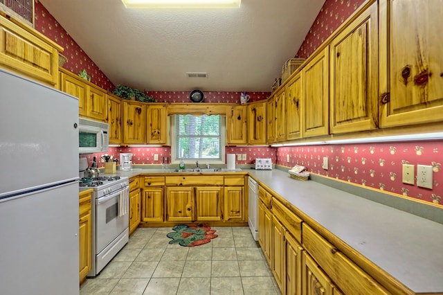 kitchen with a textured ceiling, sink, light tile patterned flooring, and white appliances