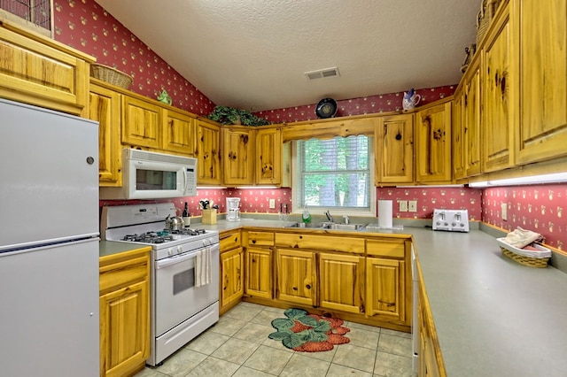 kitchen with a textured ceiling, sink, light tile patterned floors, and white appliances