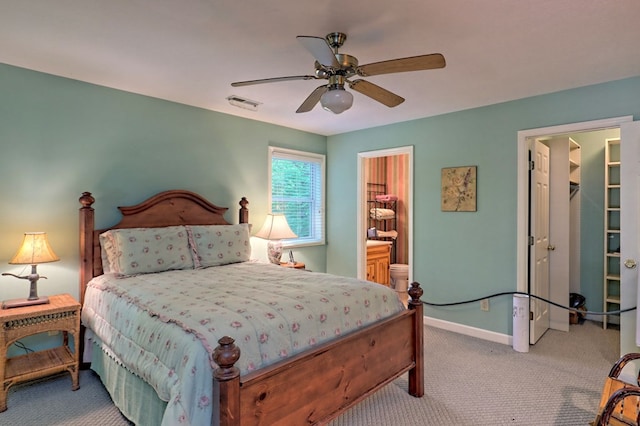 bedroom with a walk in closet, light colored carpet, ensuite bath, and ceiling fan