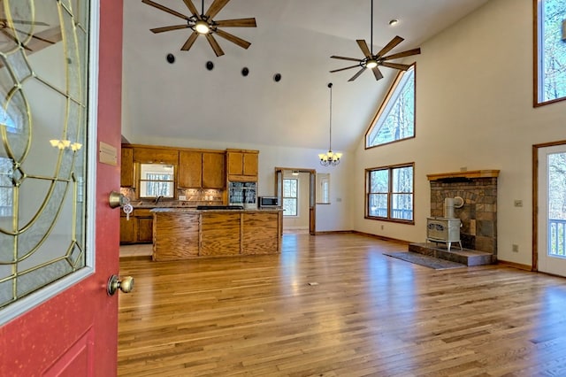 kitchen with brown cabinets, light wood-style flooring, stainless steel microwave, ceiling fan with notable chandelier, and open floor plan