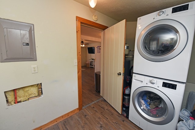 laundry room featuring ceiling fan, dark hardwood / wood-style flooring, stacked washer / dryer, electric panel, and a textured ceiling