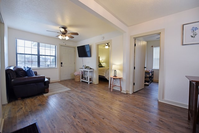 living room with a textured ceiling, ceiling fan, and dark wood-type flooring