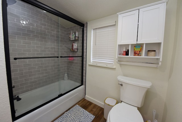 bathroom with hardwood / wood-style floors, a textured ceiling, toilet, and enclosed tub / shower combo