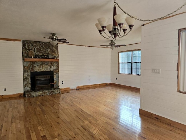 unfurnished living room with ceiling fan with notable chandelier, a stone fireplace, and wood-type flooring