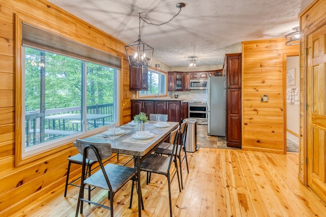 dining room featuring sink, wood walls, a chandelier, light hardwood / wood-style floors, and a textured ceiling