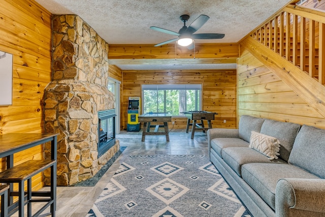 living room with wooden walls, a fireplace, ceiling fan, and a textured ceiling