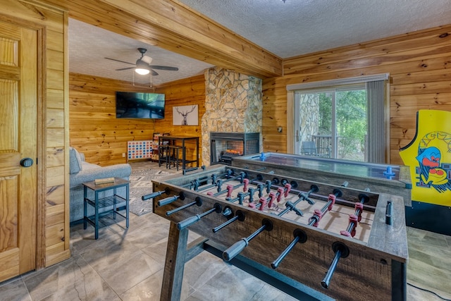 recreation room with a fireplace, ceiling fan, a textured ceiling, and wooden walls