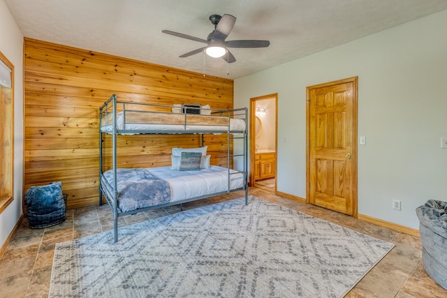 bedroom featuring ensuite bath, wooden walls, ceiling fan, and a textured ceiling