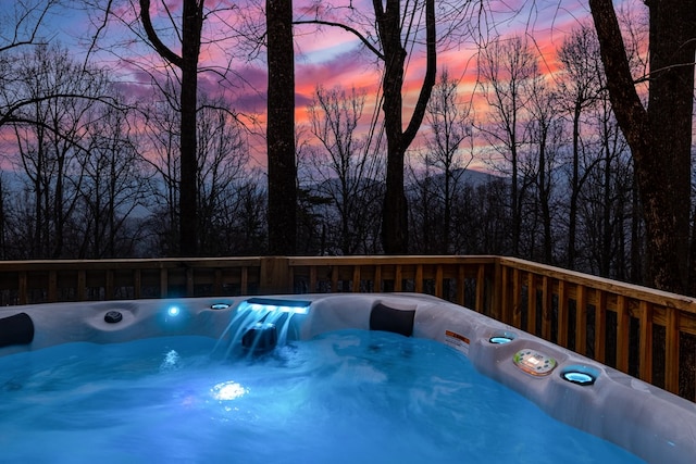 pool at dusk with a hot tub and a deck