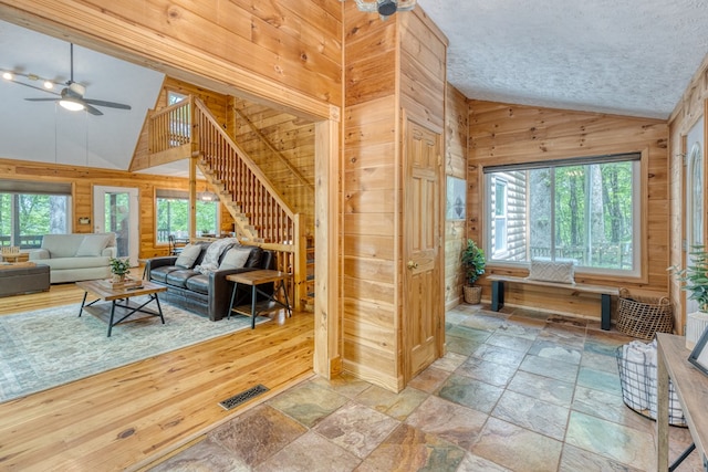 interior space featuring high vaulted ceiling, ceiling fan, and wood walls