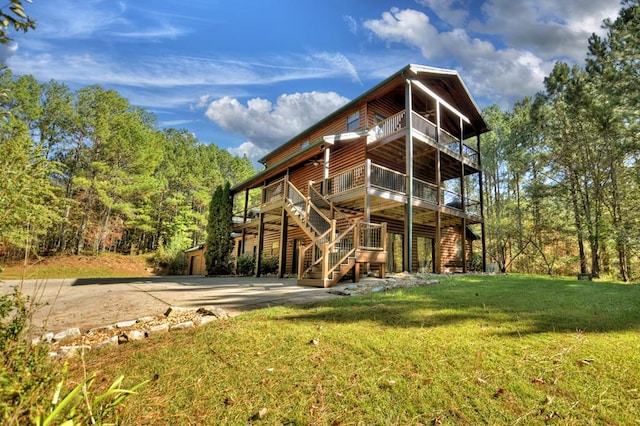 rear view of house featuring faux log siding, a wooden deck, a lawn, a balcony, and stairway