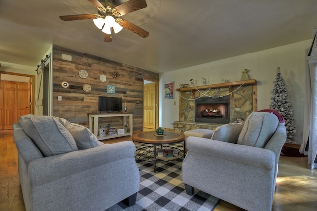 living area with wood finished floors, wood walls, a fireplace, and ceiling fan