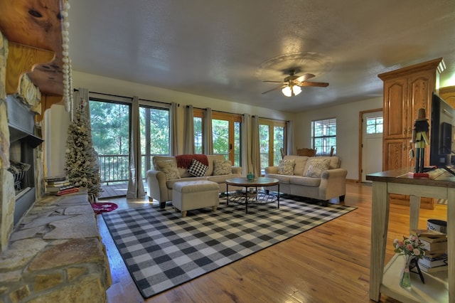 living area with a ceiling fan, a fireplace, and light wood-style floors