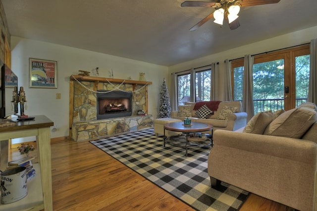 living room with baseboards, a ceiling fan, wood finished floors, and a stone fireplace