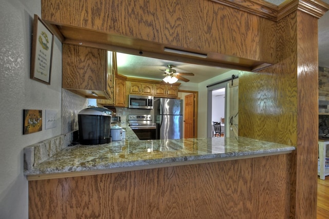 kitchen with a peninsula, a ceiling fan, brown cabinets, and appliances with stainless steel finishes