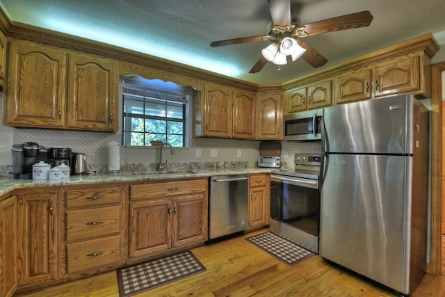 kitchen featuring light wood finished floors, stainless steel appliances, a sink, tasteful backsplash, and brown cabinets