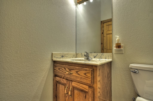 bathroom featuring a textured wall, vanity, and toilet