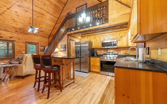 kitchen with high vaulted ceiling, wood walls, appliances with stainless steel finishes, and light hardwood / wood-style flooring