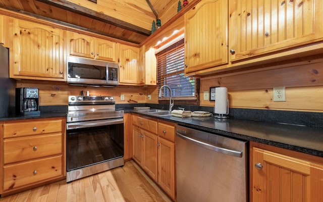 kitchen with sink, vaulted ceiling, dark stone countertops, light wood-type flooring, and appliances with stainless steel finishes