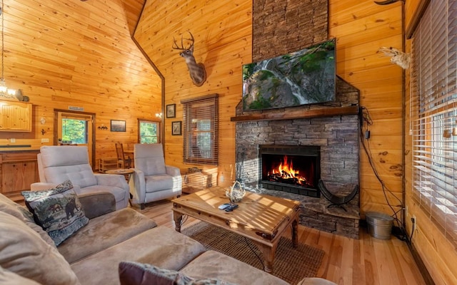 living room featuring wood walls, a fireplace, high vaulted ceiling, and light hardwood / wood-style floors