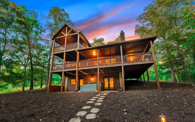 back house at dusk with a wooden deck and a hot tub