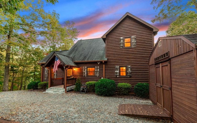 back house at dusk with a porch and a storage unit