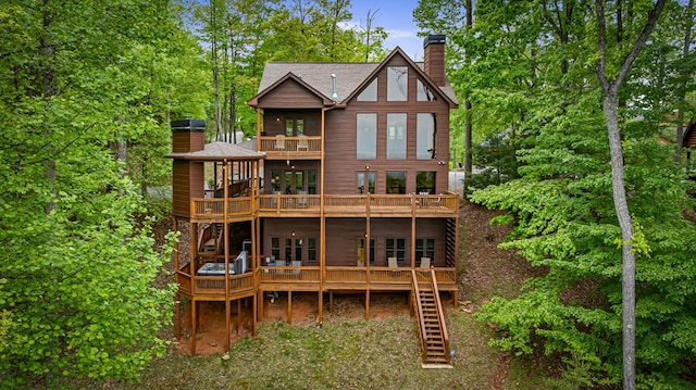 rear view of property with a balcony, a deck, roof with shingles, a chimney, and stairs