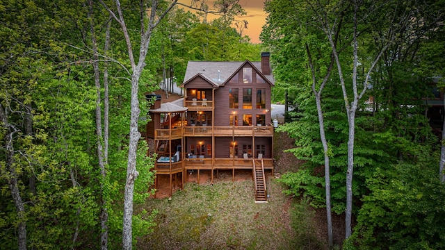 back of property at dusk with a deck, a chimney, a balcony, and stairs