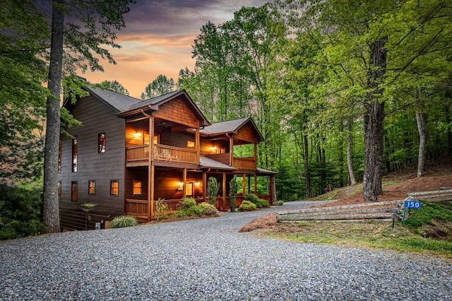 view of front of home featuring roof with shingles, covered porch, gravel driveway, and a balcony