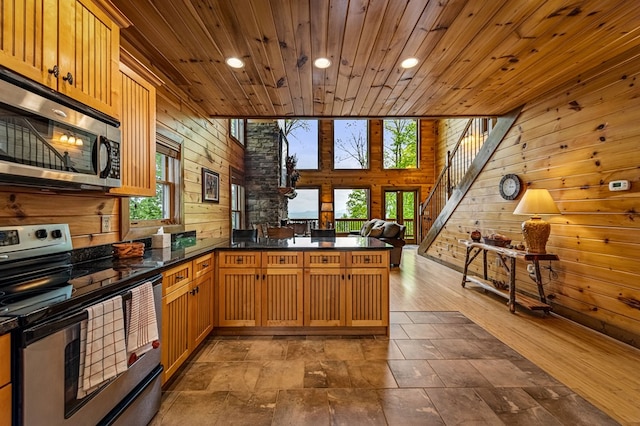 kitchen featuring appliances with stainless steel finishes, dark countertops, a peninsula, wooden walls, and recessed lighting