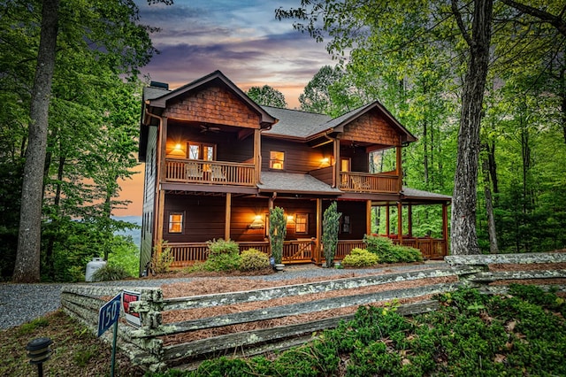 back of property at dusk with roof with shingles, covered porch, and a balcony