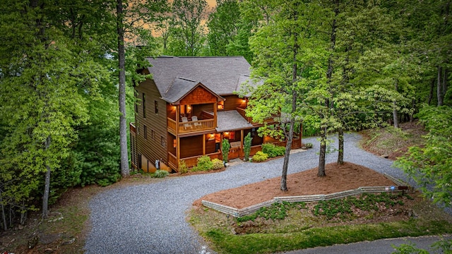 view of front of home featuring a balcony, a shingled roof, a porch, a view of trees, and driveway
