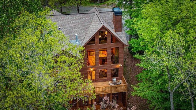 rear view of property with a chimney and roof with shingles