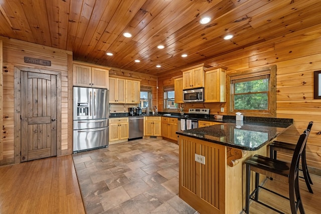 kitchen featuring wooden walls, appliances with stainless steel finishes, a sink, a peninsula, and recessed lighting