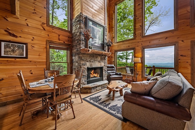 living room featuring a stone fireplace, a high ceiling, wooden walls, and wood finished floors