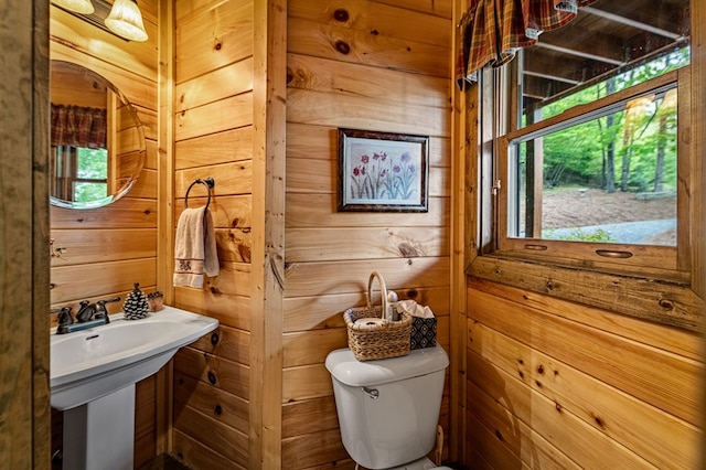 half bathroom with a sink, plenty of natural light, toilet, and wood walls
